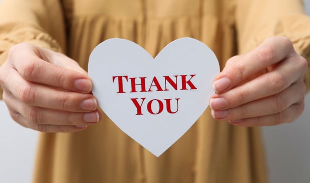 Hands holding a white heart-shaped card with 'THANK YOU' written in red letters.