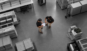 Two project managers reviewing a checklist on a clipboard, viewed from above.