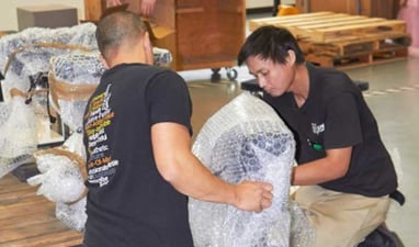 Two warehouse workers handling large bubble-wrapped items in a storage or shipping facility.