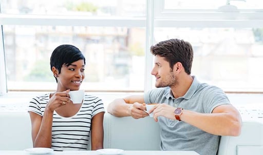 Two people conversing at a table while holding cups of coffee.