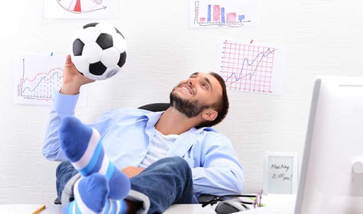 A man sitting in an office, holding a soccer ball and smiling.