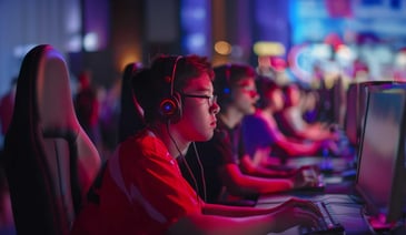 A focused young gamer wearing a headset participates in an esports event, surrounded by other players in a neon-lit setting.