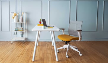 A minimalist home office with a white desk, yellow chair, and shelving.