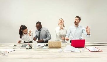 Office workers expressing joy at their desks with laptops and paperwork scattered on the table.