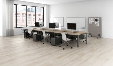 A modern minimalist office space with multiple workstations along a wooden desk, white chairs, and large windows overlooking an urban setting.