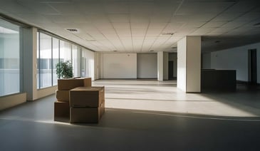 An empty office space with cardboard boxes stacked on the floor near large windows.