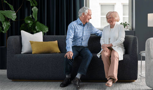 Two seniors sitting on a dark charcoal Carolina Elara sofa.