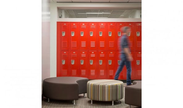 Orange lockers in a hallway with circular seating nearby, creating an in-between space for informal gatherings.