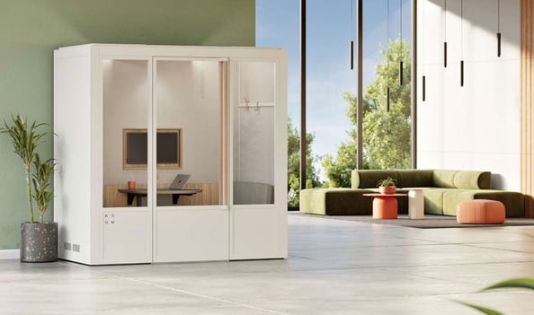 A modern, glass-enclosed private workspace pod with comfortable furnishings in a bright office environment.