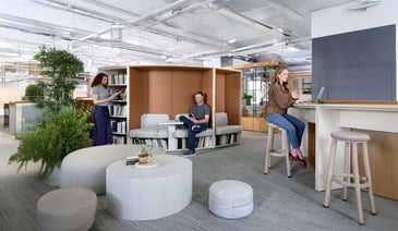 A modern open office space featuring comfortable seating, plants, and individuals working in collaborative and private areas.