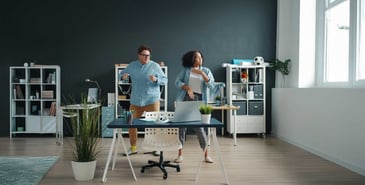 Two colleagues taking a dance break at their modern office desk.