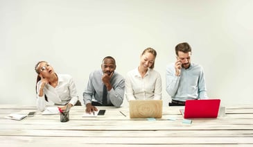 Four diverse professionals sitting together, each engaged in different activities - one looking up thoughtfully, one in contemplation, one smiling while reading, and one talking on the phone.
